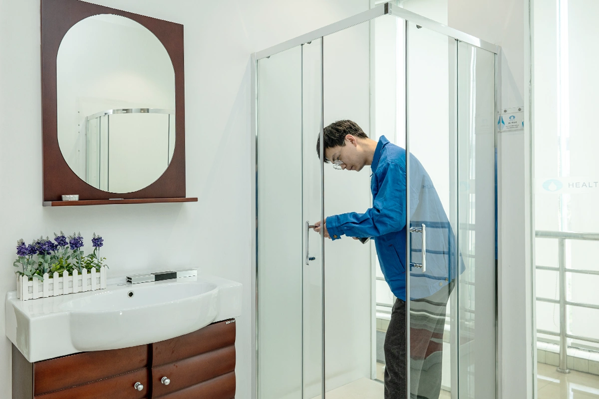 Man testing a frameless glass sliding shower door with chrome handles in a bright bathroom showroom
