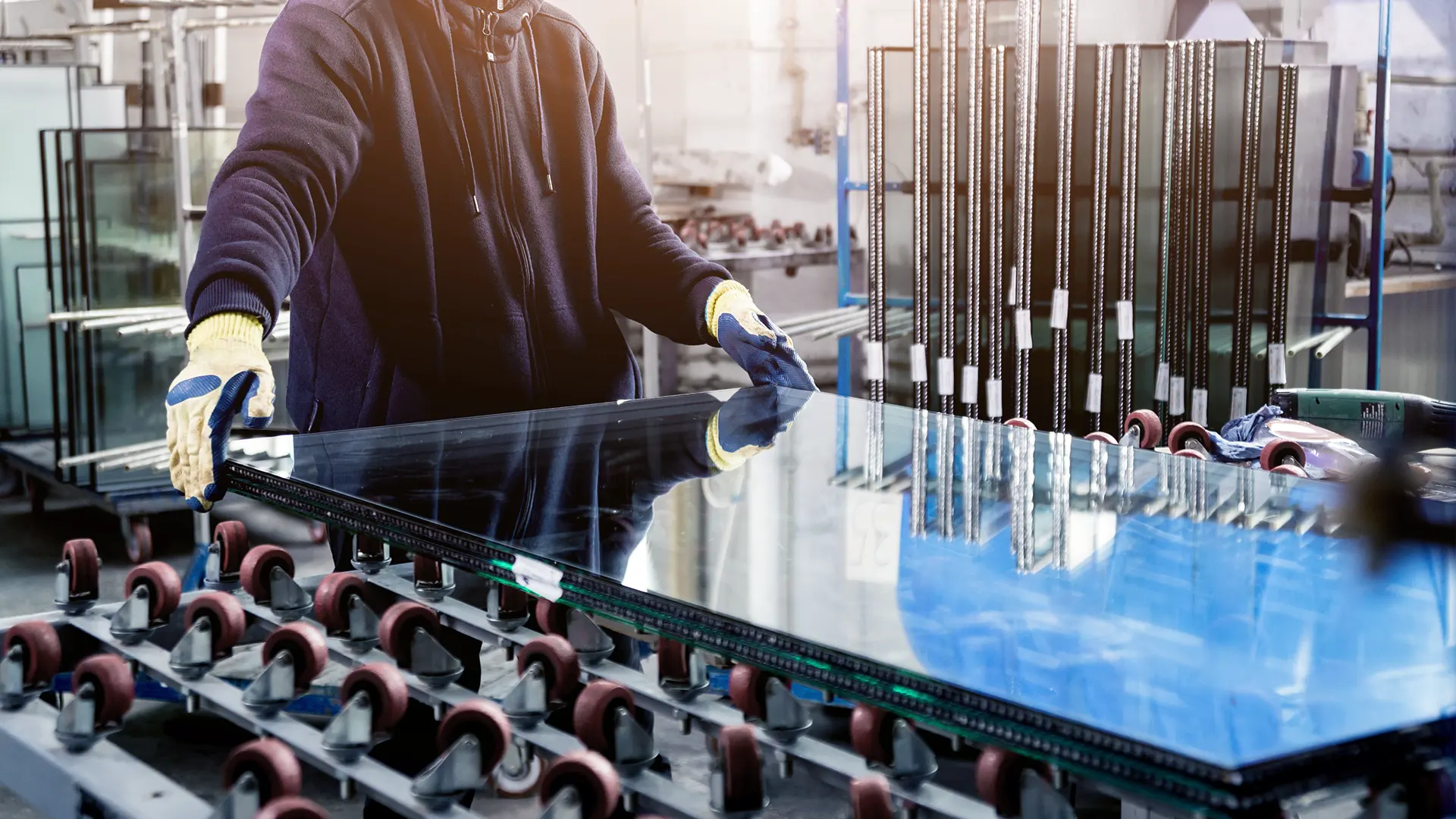 Factory worker in gloves guiding a large glass panel on the roller conveyor of the glass processing production line