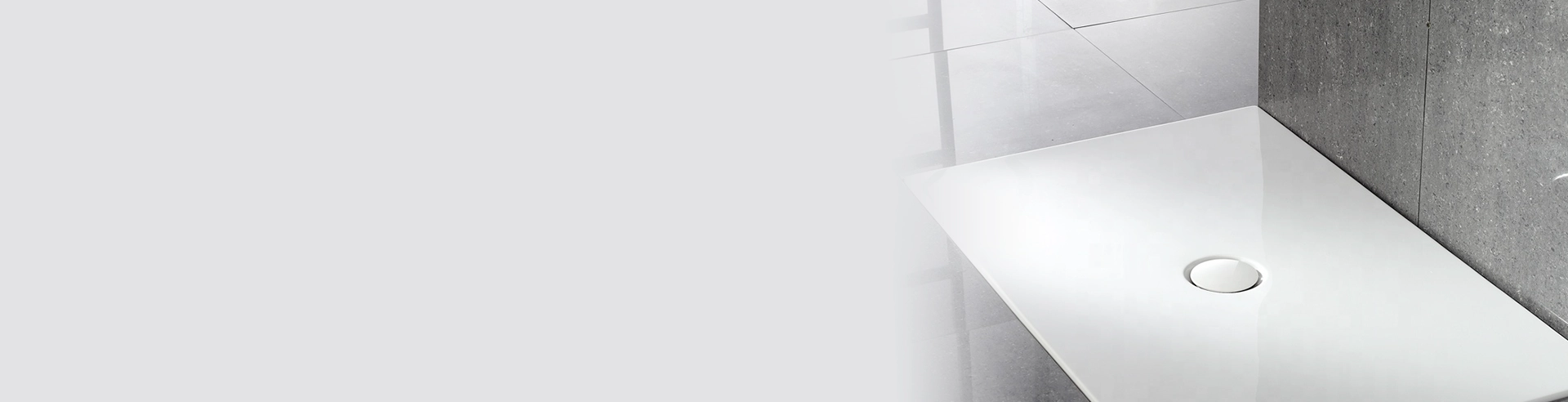 Glossy white rectangular shower tray with central circular drain on gray tiles against a concrete wall, banner image