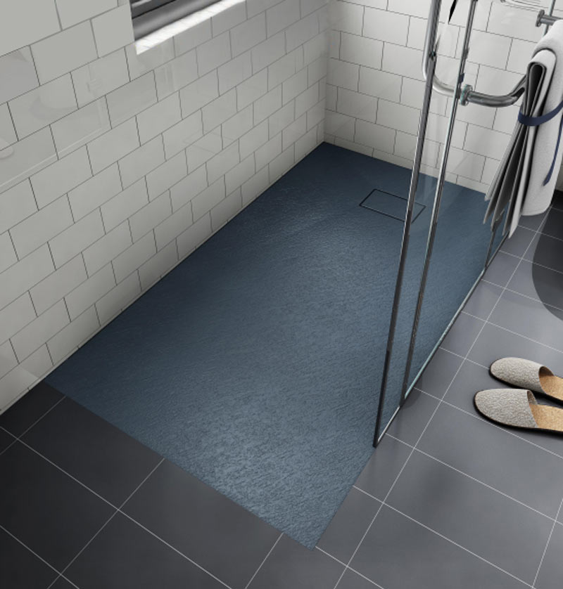 Blue-gray textured shower base with square drain cover installed in a subway-tiled bathroom with glass door