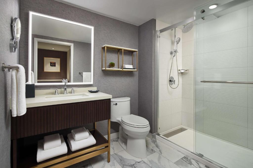 Modern hotel bathroom with glass sliding shower door, rain shower head, LED mirror vanity and marble floor
