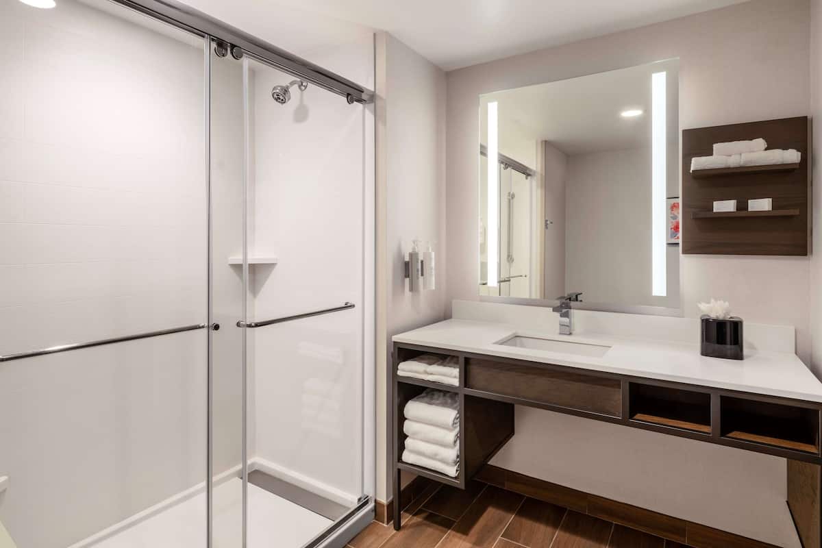 Hotel bathroom with frameless glass sliding shower enclosure, chrome grab bars, and marble vanity