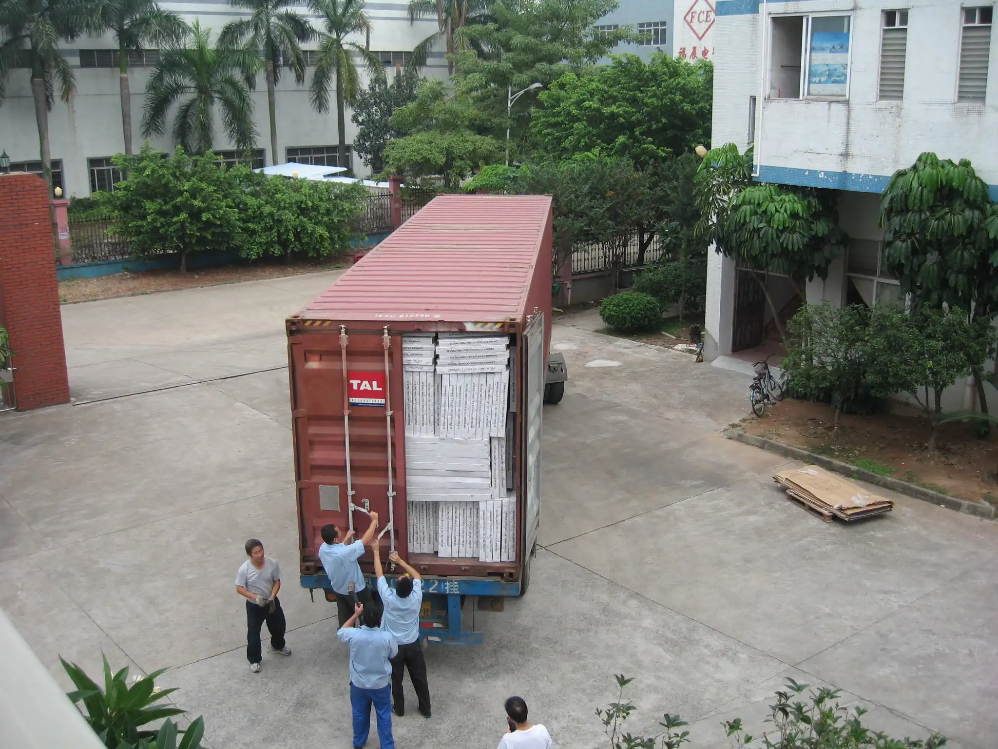 Factory workers loading stacked white packages into a red shipping container
