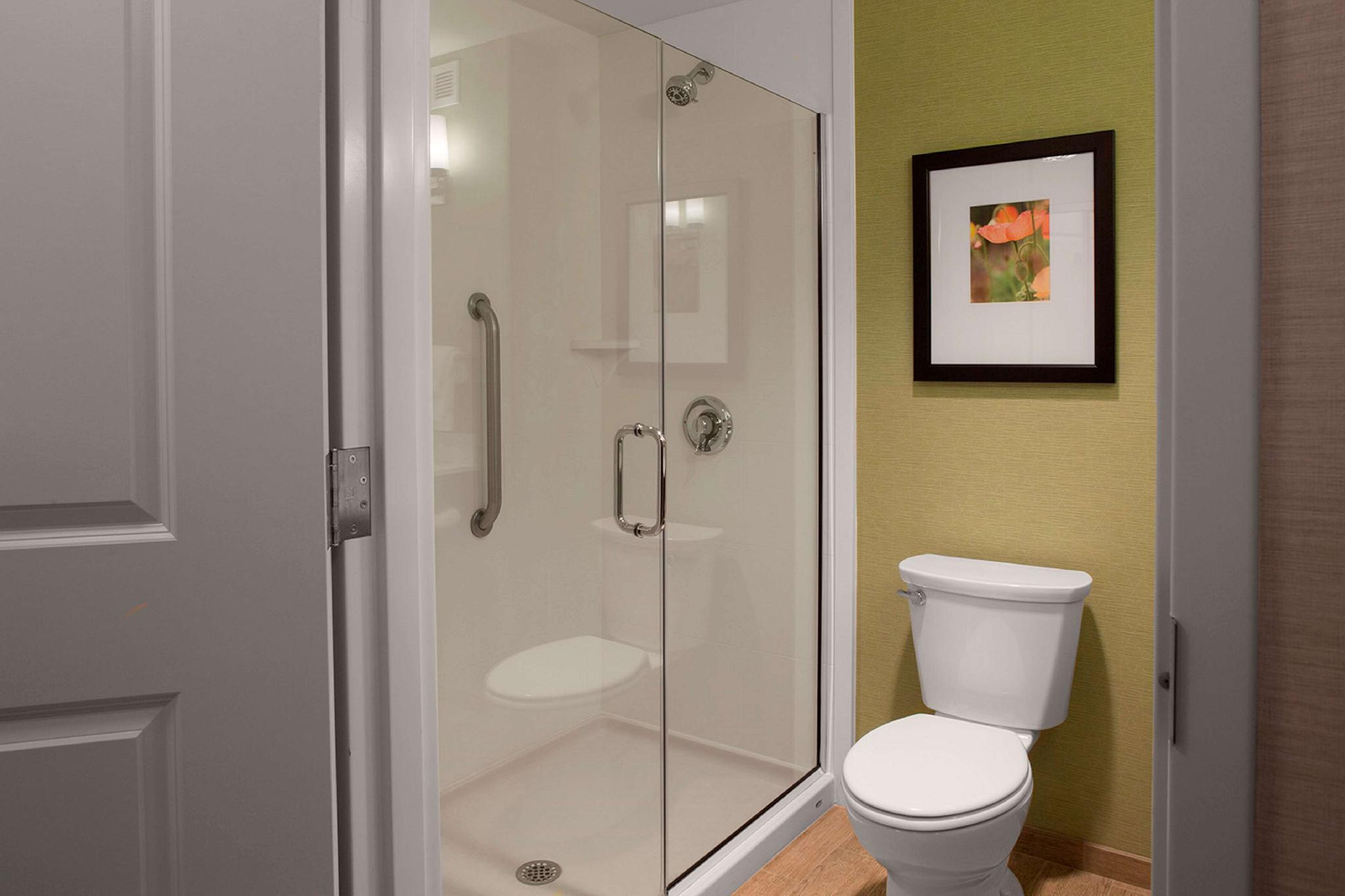 Accessible hotel bathroom with glass sliding walk-in shower, built-in seat, grab bar and white toilet