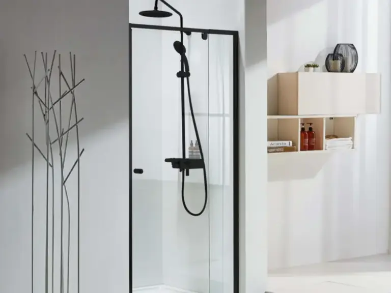 Slim black framed glass shower door with matte black rainfall showerhead and shelf in a minimalist white tiled bathroom