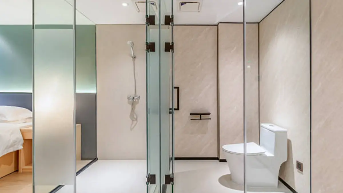 Frameless glass shower door with bronze hinges installed beside a vanity in a hotel bathroom