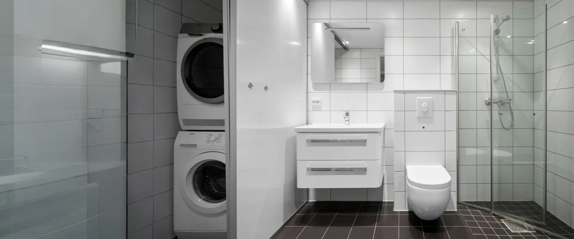 Curved glass shower door in a compact apartment bathroom with wall-hung vanity, toilet and stacked laundry unit