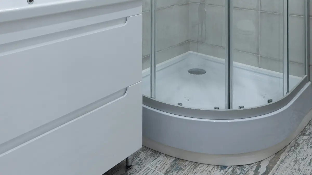 Semi-circular white corner shower base with chrome posts and tempered glass panels