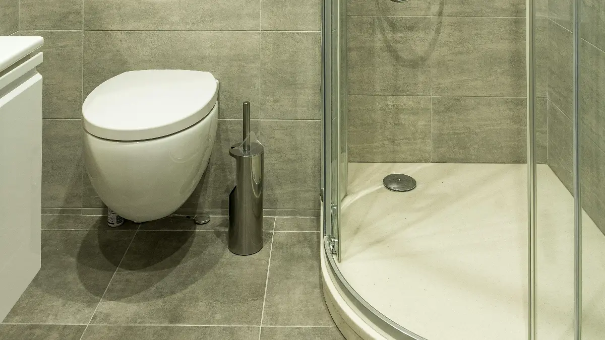 Curved corner glass shower enclosure with beige acrylic base and chrome frame in a tiled bathroom