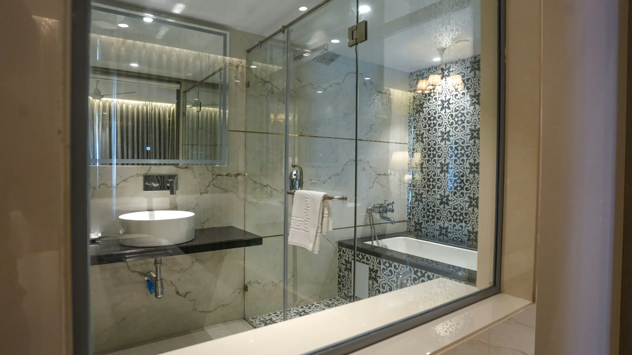 Luxury bathroom with marble walls, glass shower, vessel sink, and bathtub with blue patterned tiles.