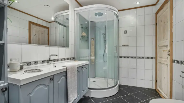 Modern bathroom with a curved glass corner shower, blue vanity cabinet, and white tiled walls.
