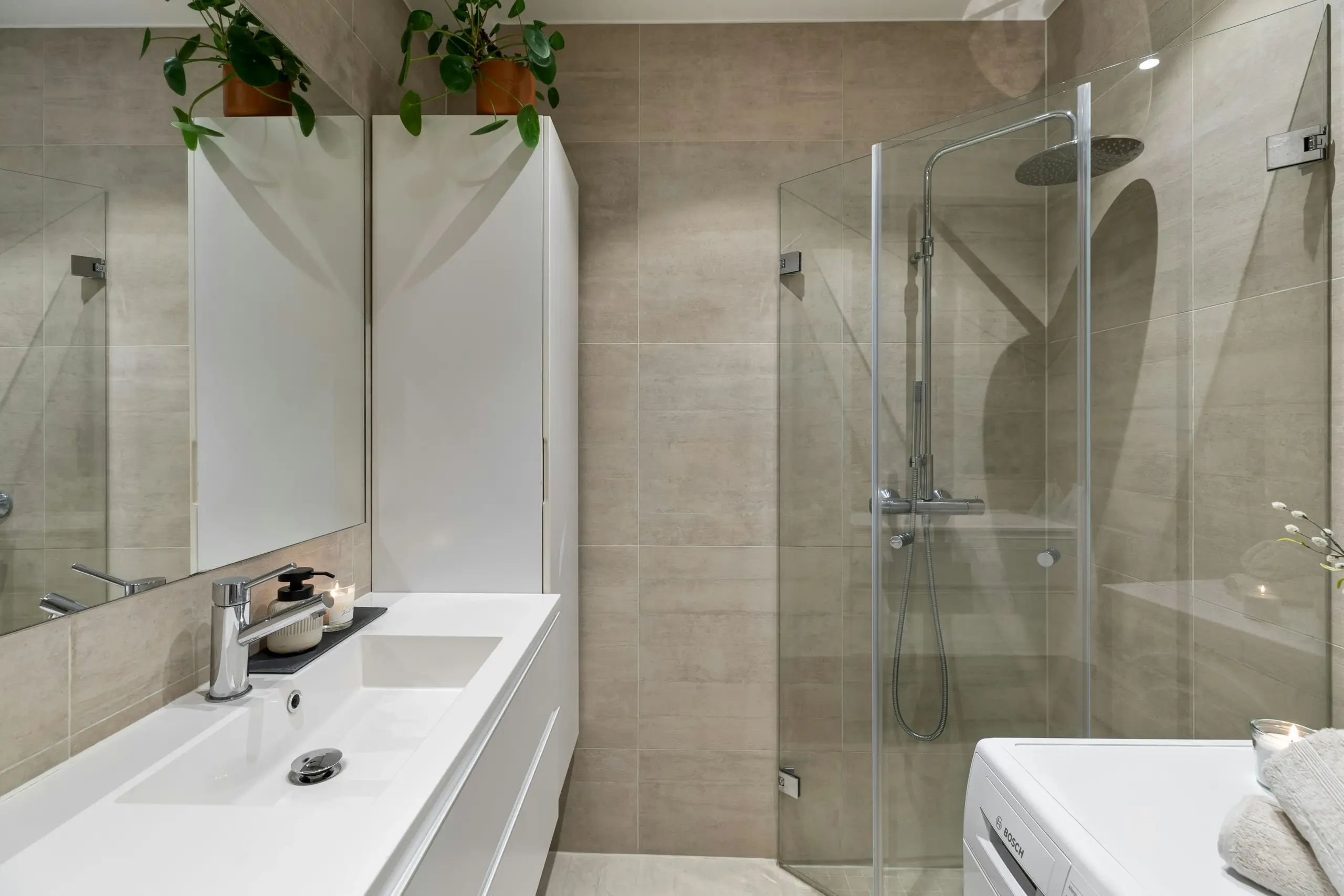 Modern Bathroom with Glass Shower and White Vanity Modern bathroom with white vanity, glass shower, beige tiles, and potted plants
