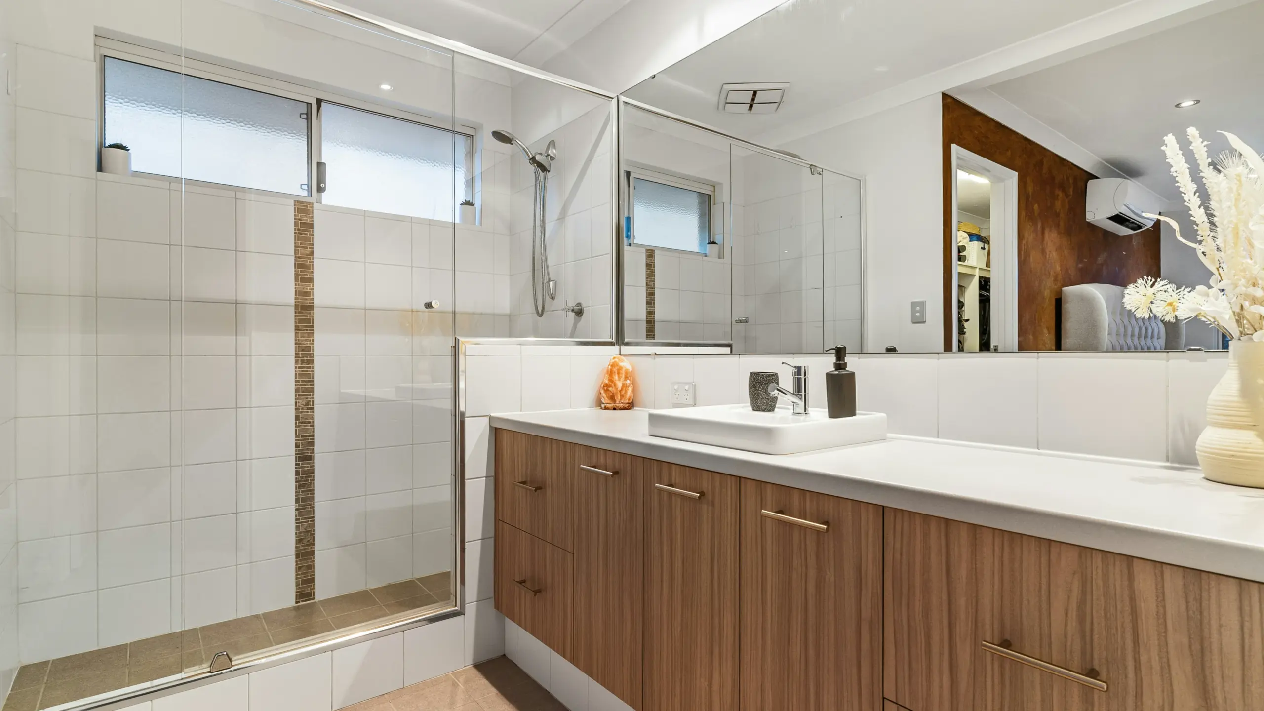 Modern bathroom featuring a sliding enclosure and a wooden vanity with white countertops.