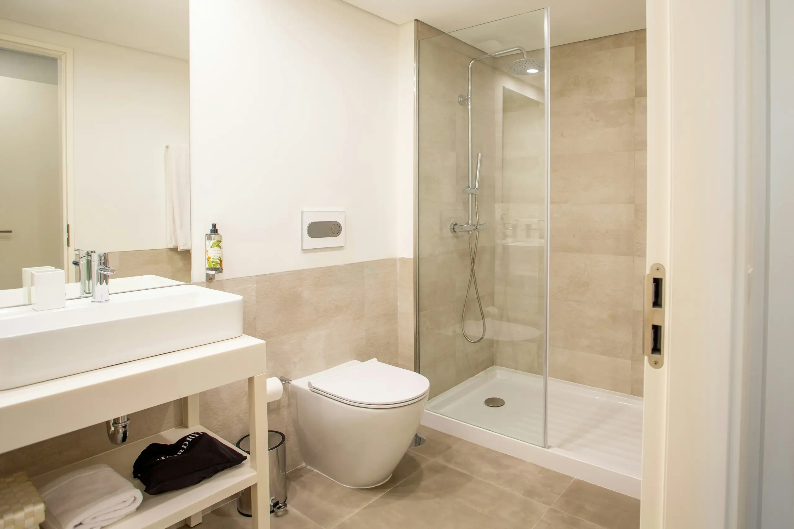 Contemporary bathroom featuring glass shower enclosure, white vessel sink, and wall-mounted toilet with beige stone tile