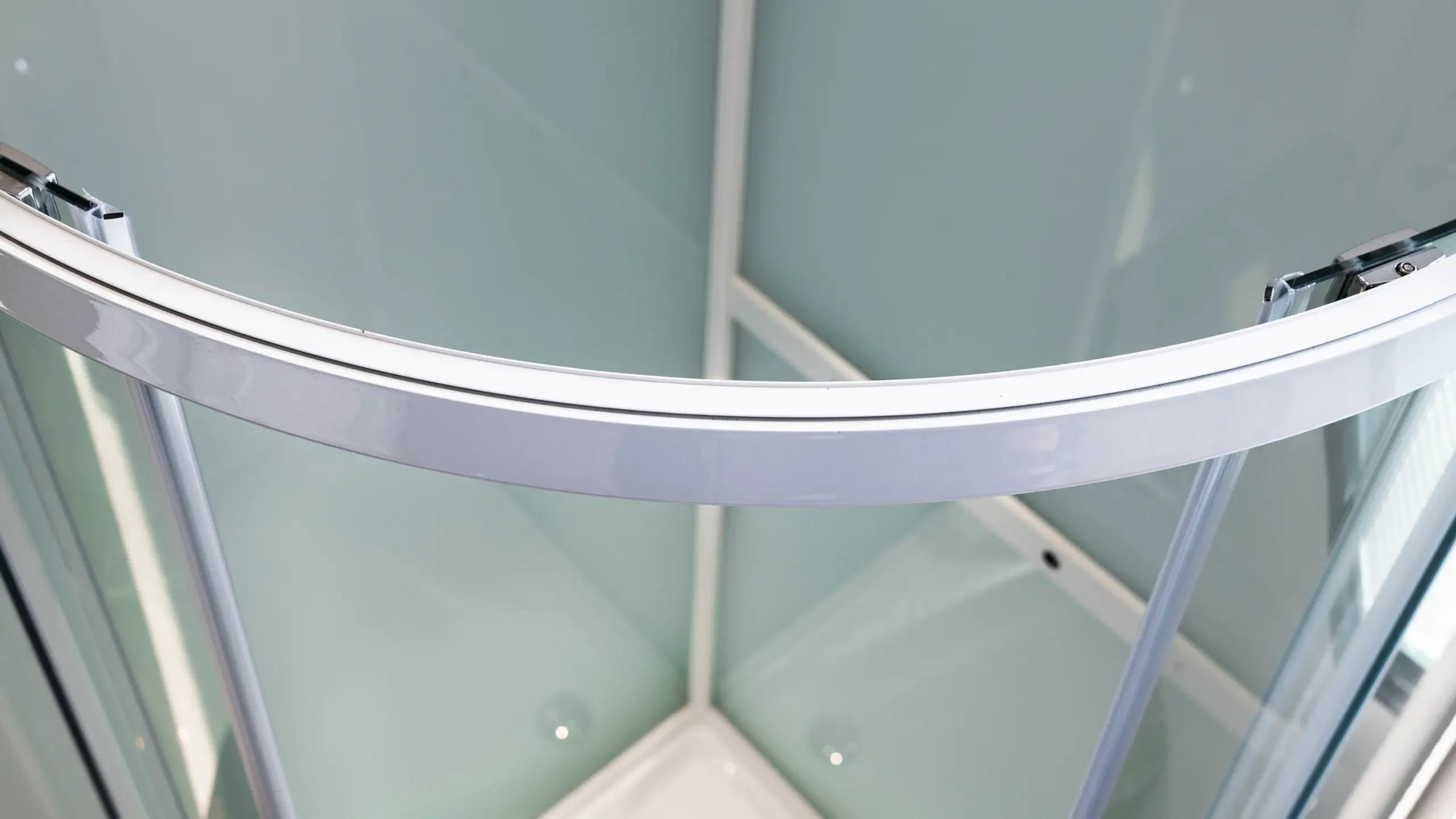 Close-up of the curved white frame and frosted glass panels of a modern corner shower enclosure.