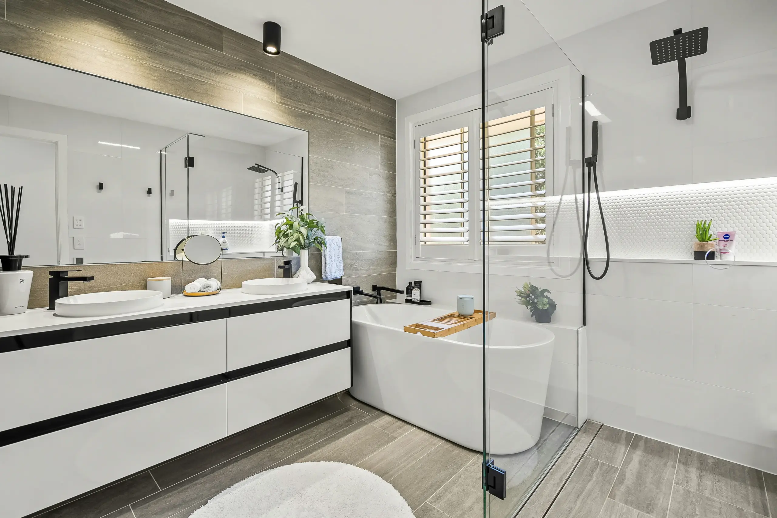 Modern Luxury Bathroom with Freestanding Tub and Double Vanity Spacious modern bathroom featuring a white freestanding tub, dual sink vanity, and glass-enclosed shower with gray tile accents.