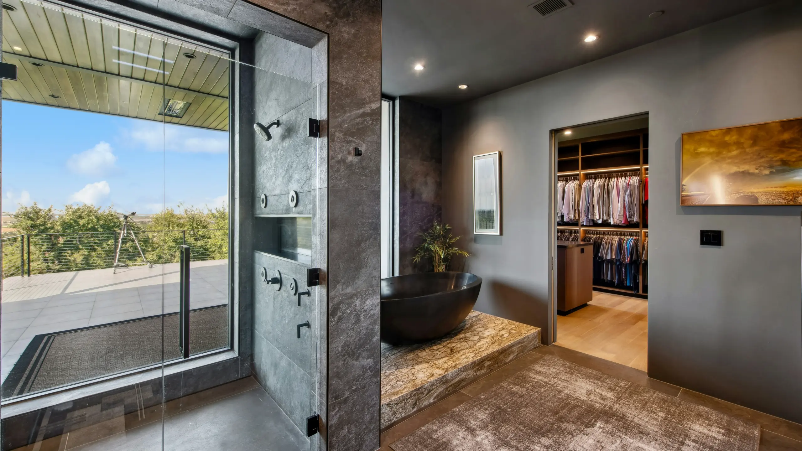 Luxurious modern bathroom featuring a freestanding black bathtub, glass walk-in shower with outdoor deck view, and open walk-in closet