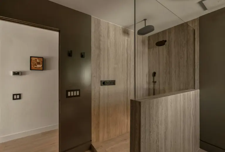 Luxury bathroom with travertine stone walls, glass shower enclosure, and matte black rainfall shower fixtures