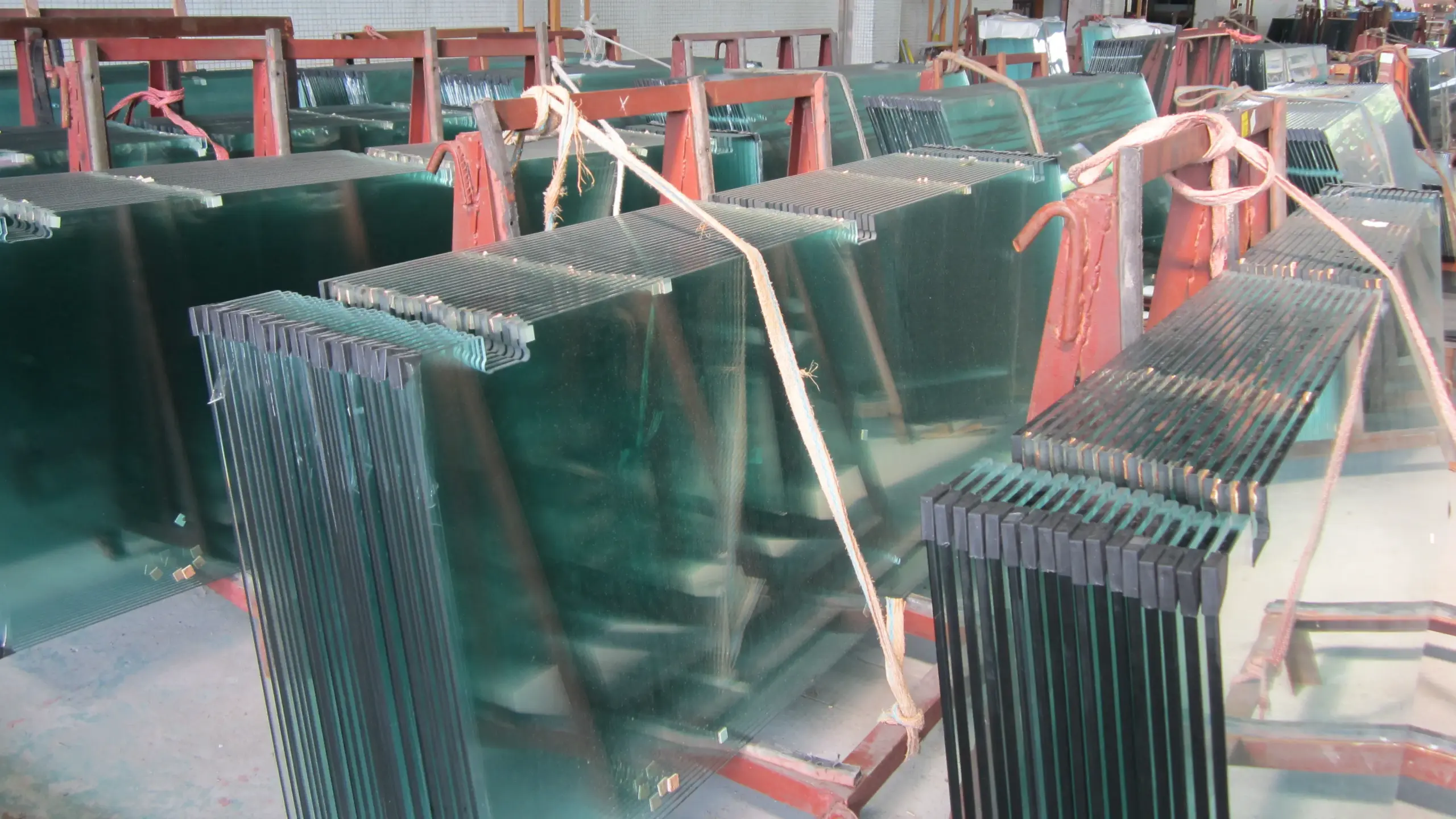 S6 Glass Material Industrial Glass Panel Storage Stacks of S6 glass panels stored on red metal racks in a factory warehouse, tied with ropes for transport