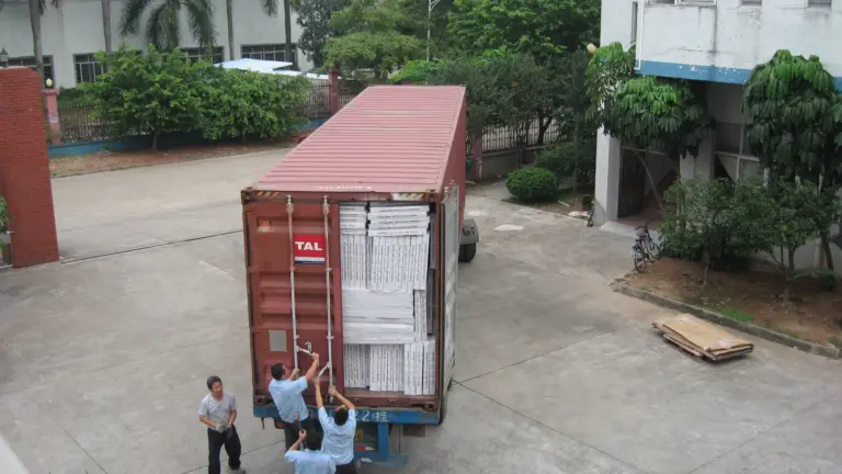Workers closing the doors of a red shipping container packed with white boxes at a factory.